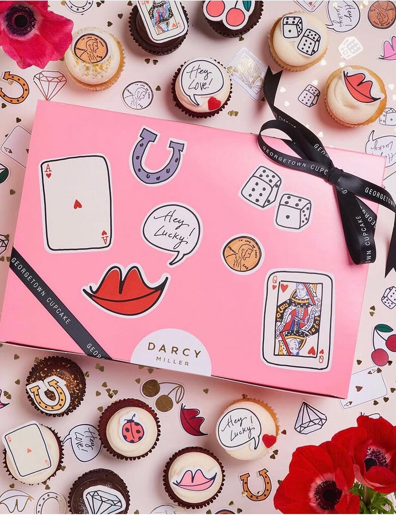 Pink gift box with playful illustrations surrounded by decorated cupcakes