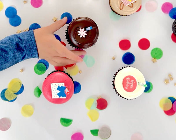 Hand reaching for a birthday cupcake surrounded by colorful confetti