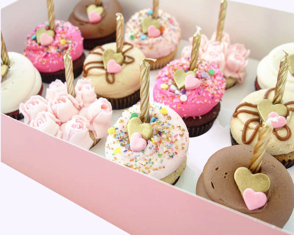 Decorated cupcakes with heart toppers and candles arranged in a gift box