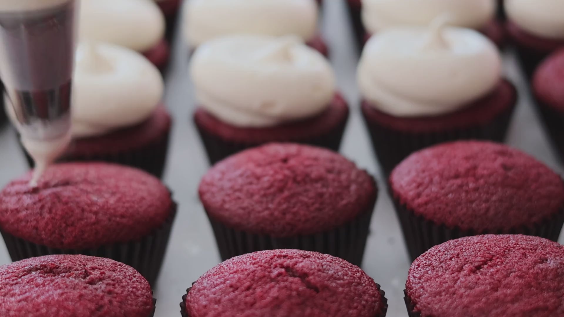 Red velvet cupcakes being topped with cream cheese frosting