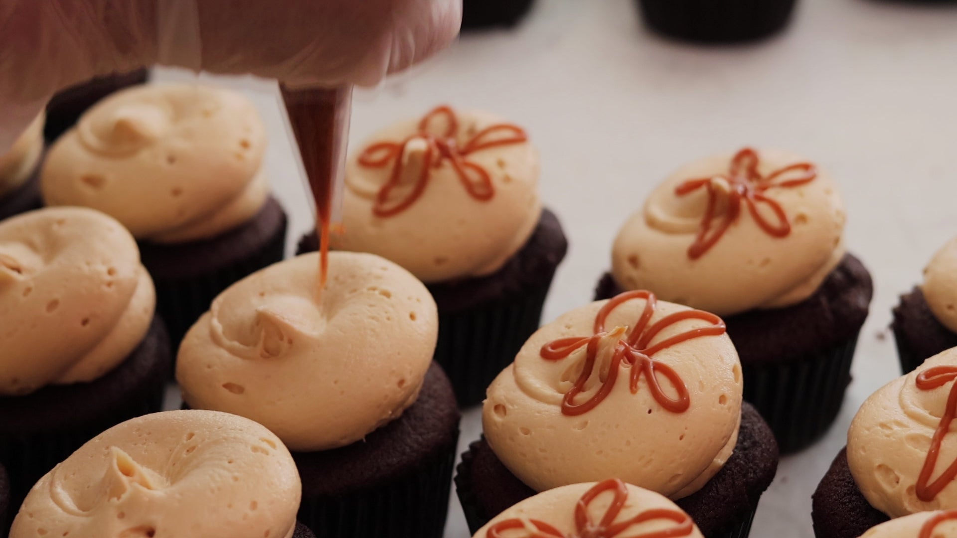 Caramel drizzle being piped onto frosted chocolate cupcakes